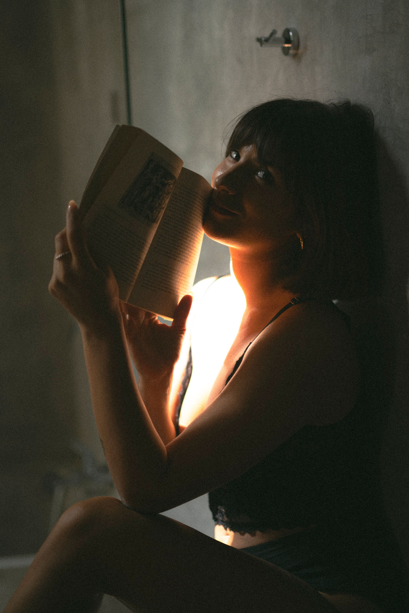 Emanuela reading a book by candlelight against a dark wall